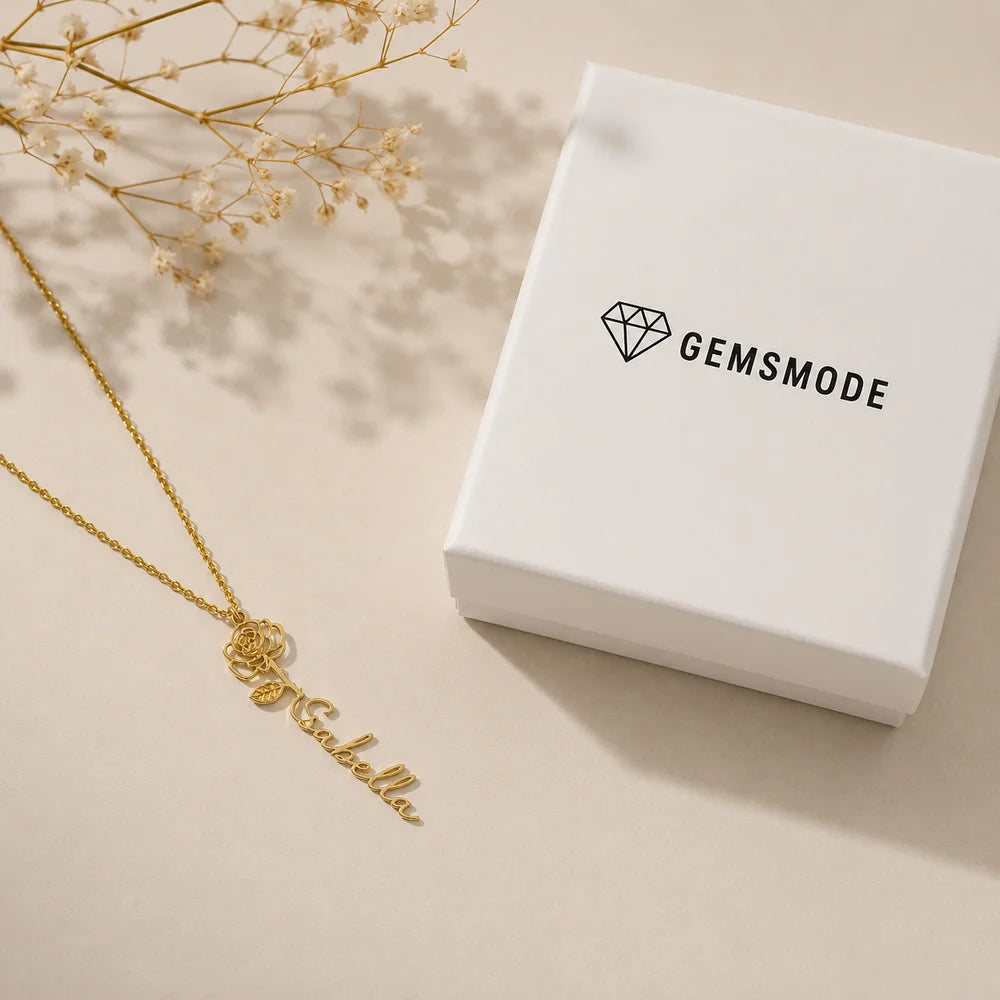Personalized gold name necklace with birth flower charm, styled flat lay with gift box