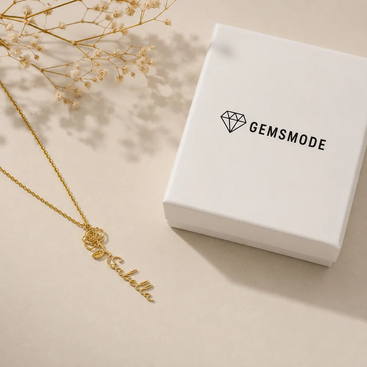 Personalized gold name necklace with birth flower charm, styled flat lay with gift box