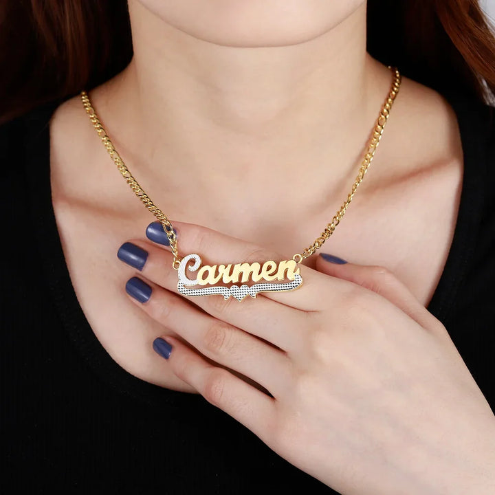 Close-up of model holding Double Plated Cursive Name Necklace in Gold with heart design element and Figaro chain.