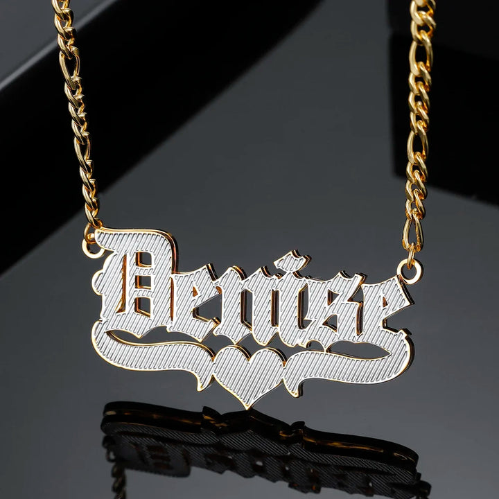 Double Plated Old English Name Necklace in Gold with Figaro Chain on Black Surface