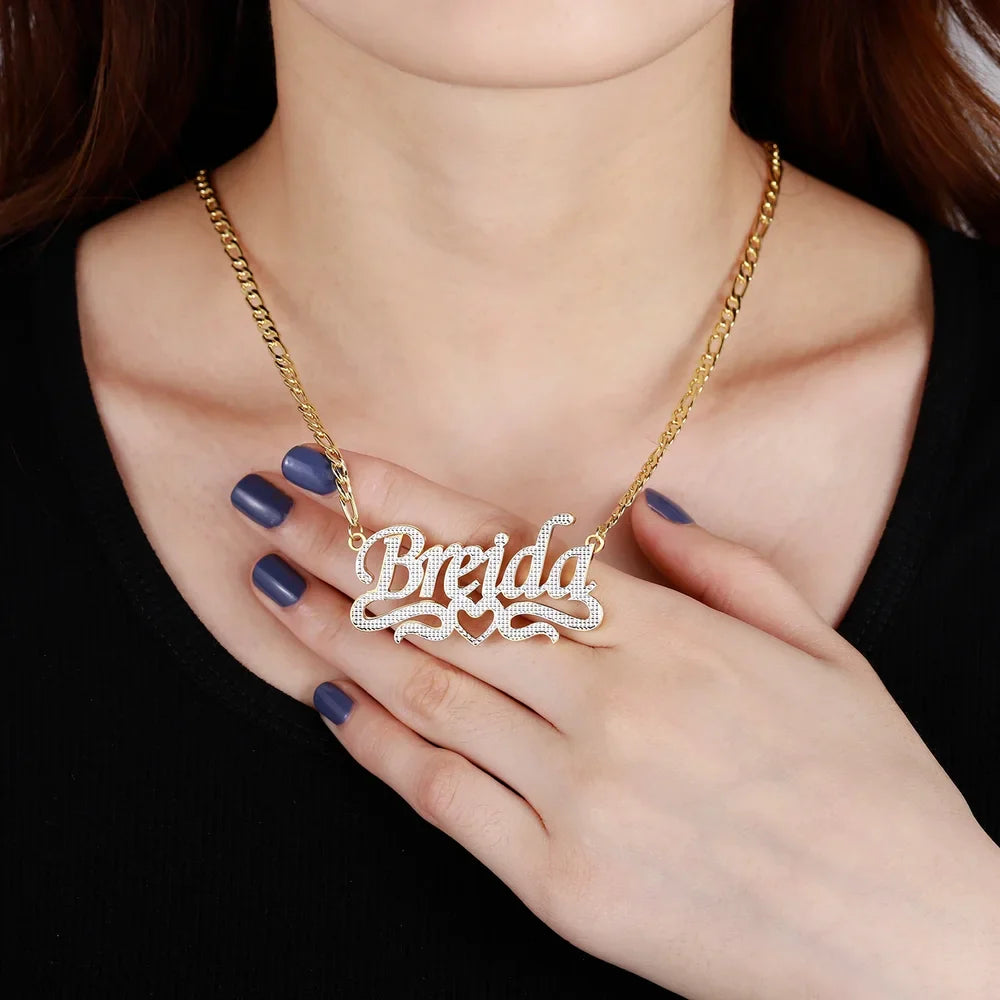 Double Plated Script Name Necklace in gold with Figaro chain worn by a model, with hand touching the necklace.