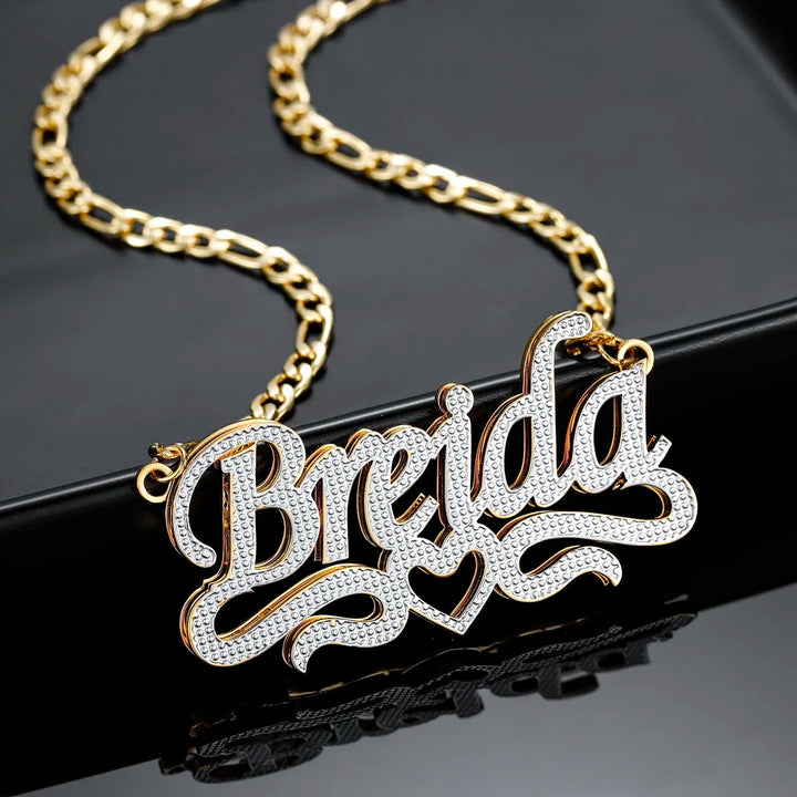 Double Plated Script Name Necklace in gold with Figaro chain displayed on a black background.