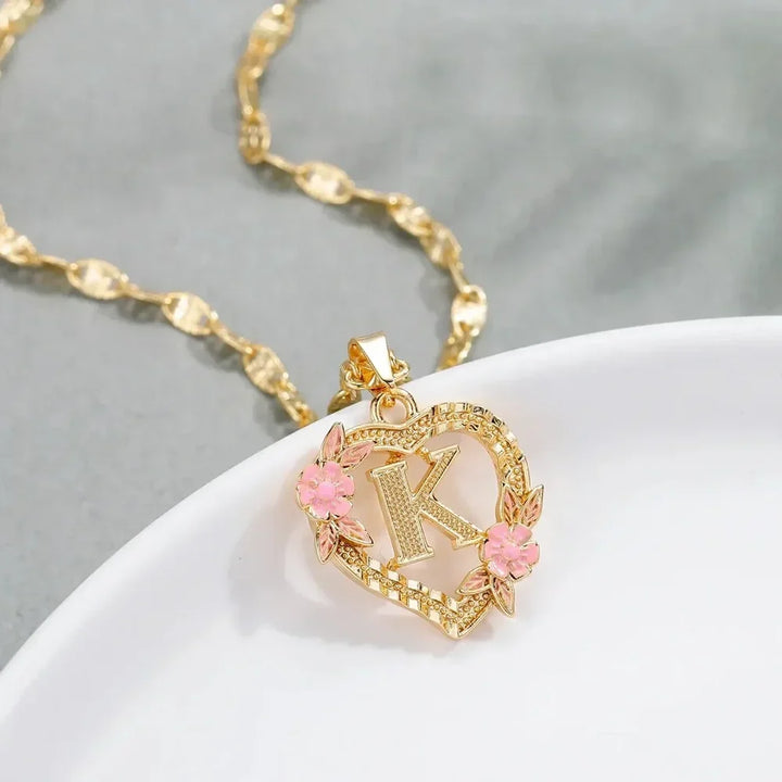 Close-up of gold Personalized Floral Initial Necklace with pink flowers and initial 'K', displayed on a dish.