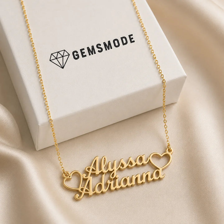 Personalized double heart name necklace in gold with custom names "Alyssa" and "Adrianna" displayed on satin fabric