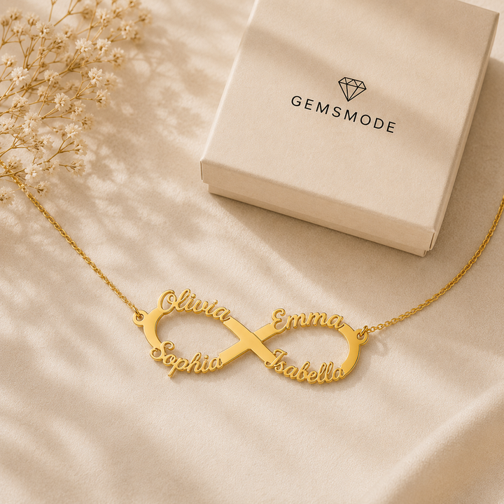 Personalized infinity name necklace in gold with four custom names displayed on fabric beside a gemsmode gift box