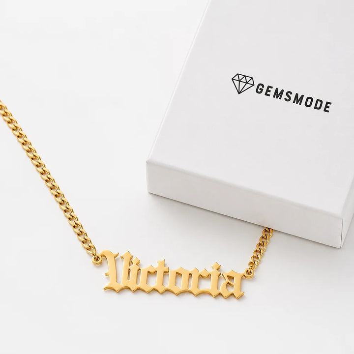 Personalized old english name necklace in gold with custom name "Victoria" displayed beside a gift box